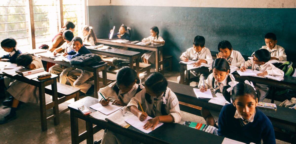 Picture of a traditional classroom with elementary school children, some studying quietly, others playing